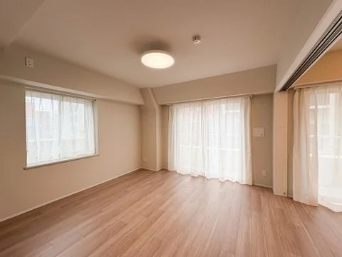 空のリビングルーム、木製の床、大きな窓とカーテン、照明器具あり。