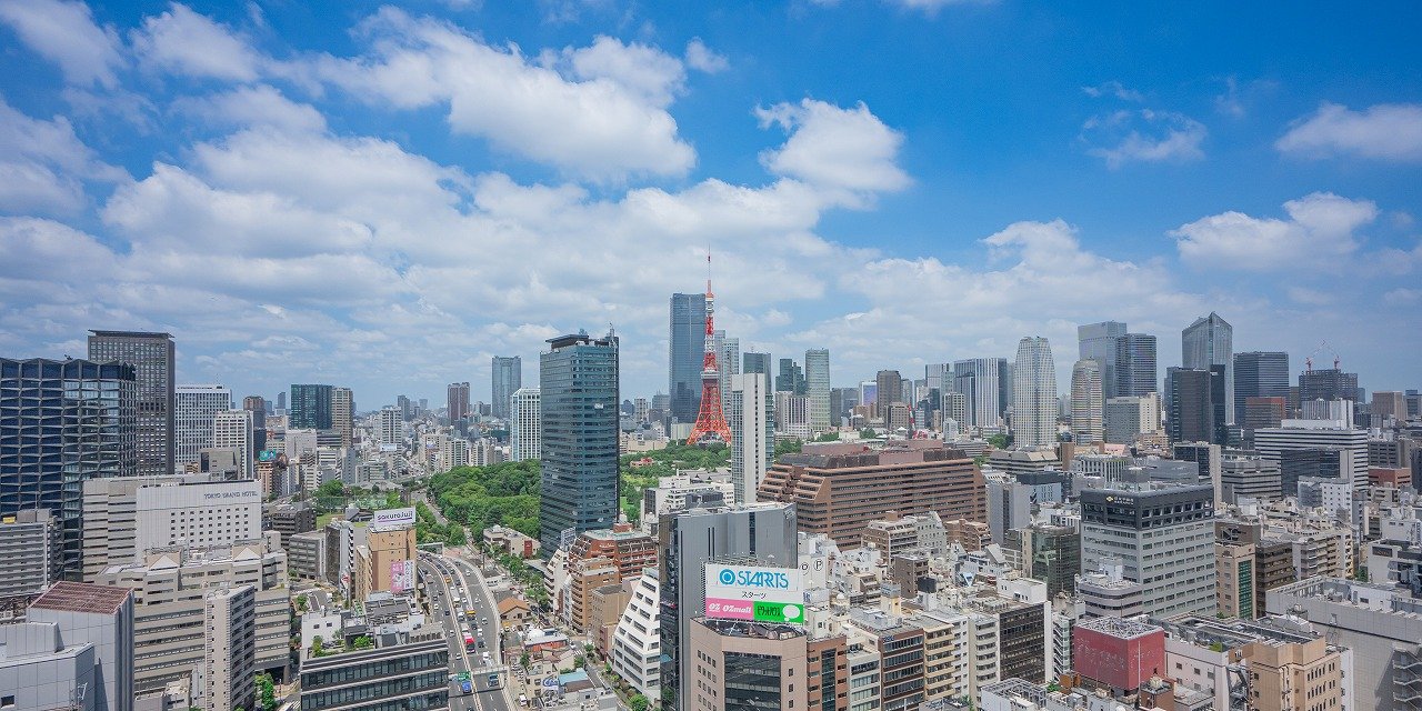 東京の都市のパノラマビュー。高層ビルと東京タワーが見える青空の下、多くの建物が立ち並んでいる。