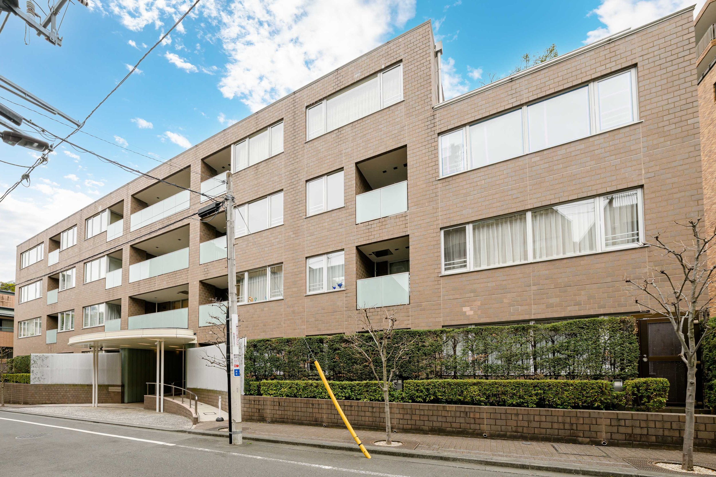 ブラウンの多層集合住宅の建物。前には歩道と数本の木。空は晴れている。