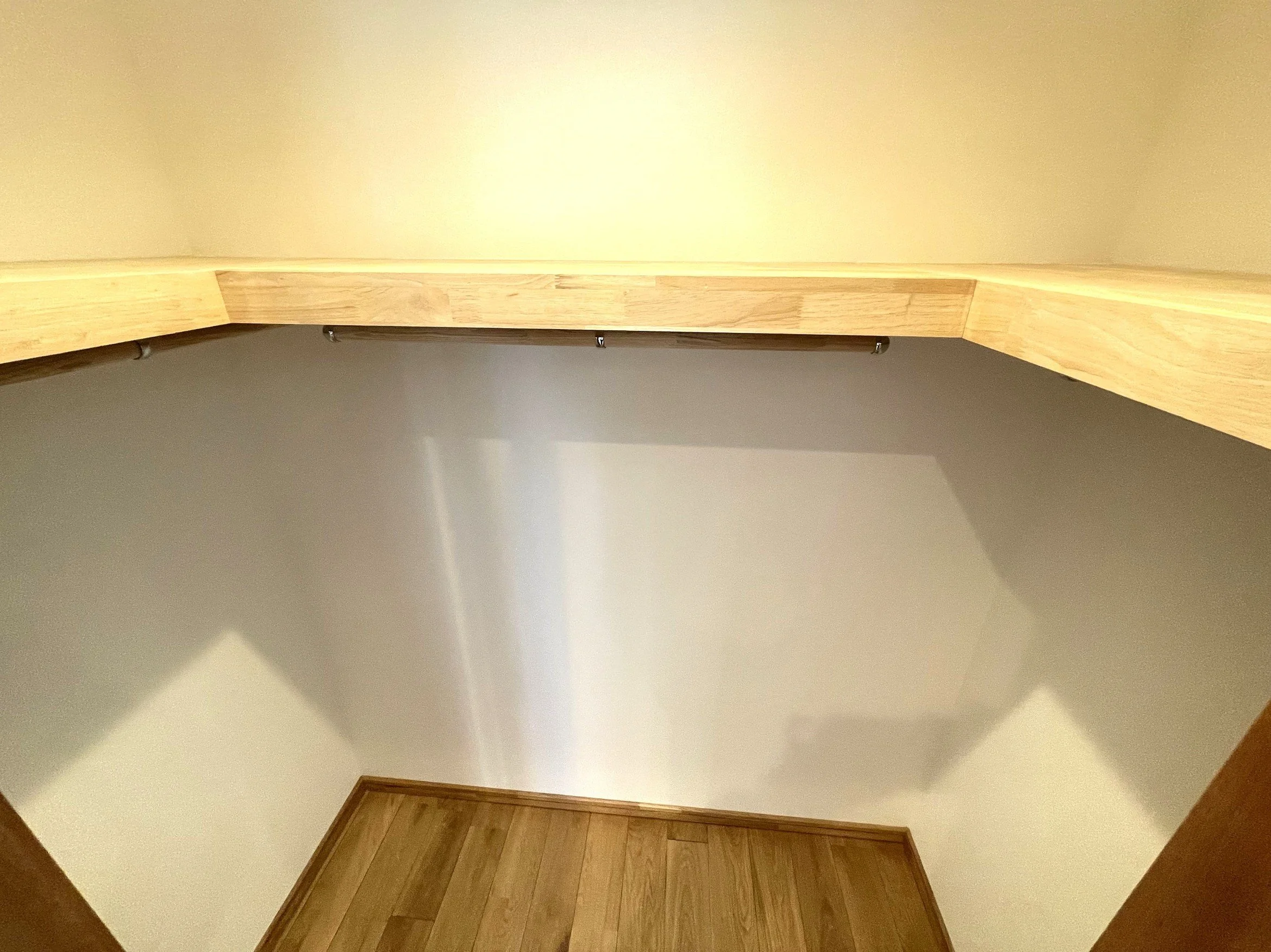 部屋のコーナーにある壁と木製のフロア。壁は白色で、木製の飾り棚が設置されている。