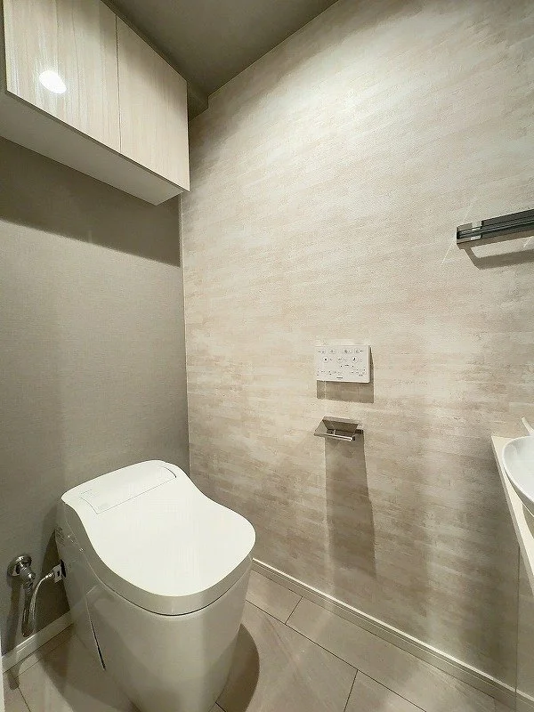 洗面所にあるトイレと壁に設置されたコントロールパネルと棚。