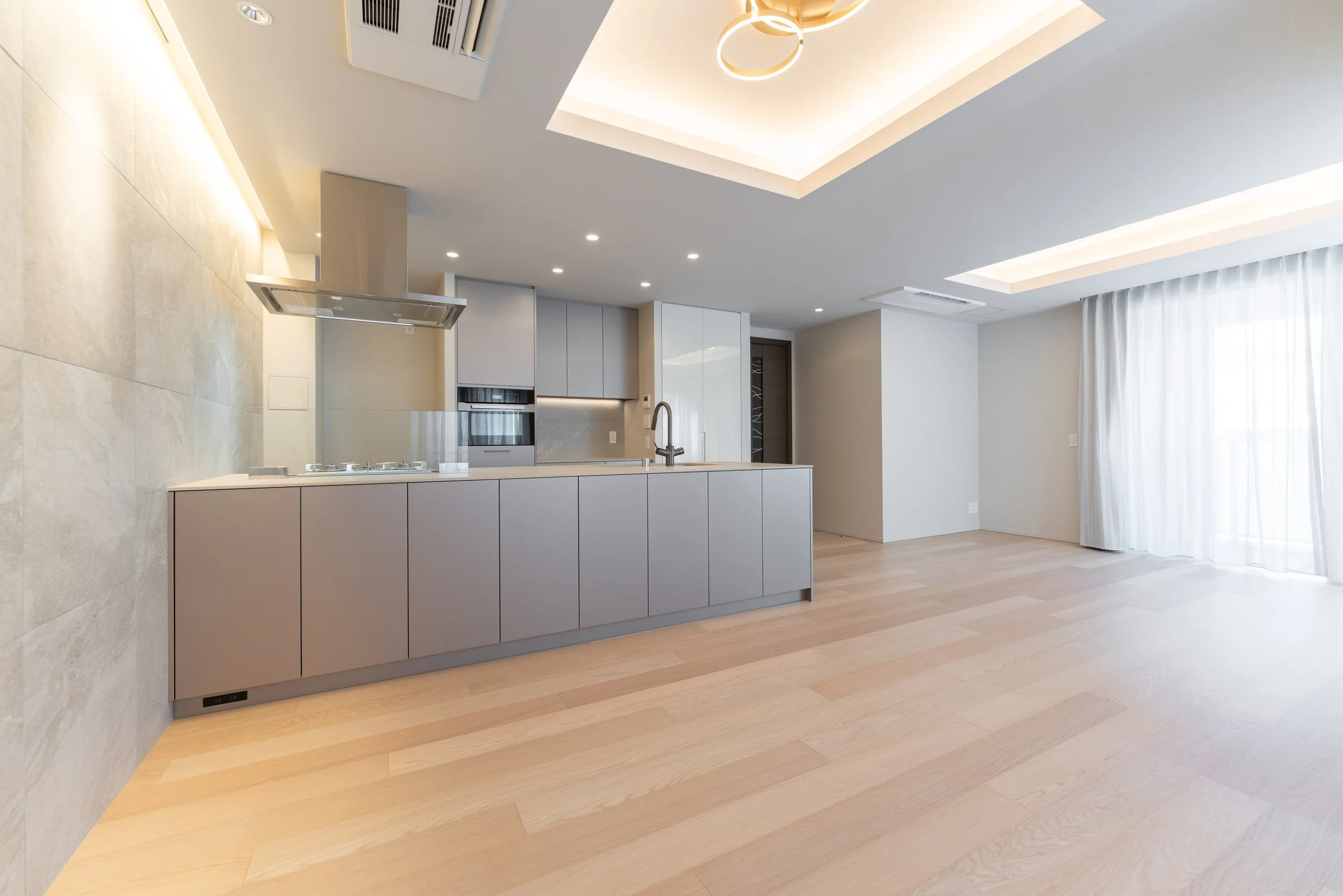 明るくてシンプルなリビングとキッチンのインテリア、木製の床と白い壁、大きな窓に白いカーテンあり