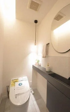 白い壁のトイレルームに洗浄便座付きトイレと鏡と棚がある。