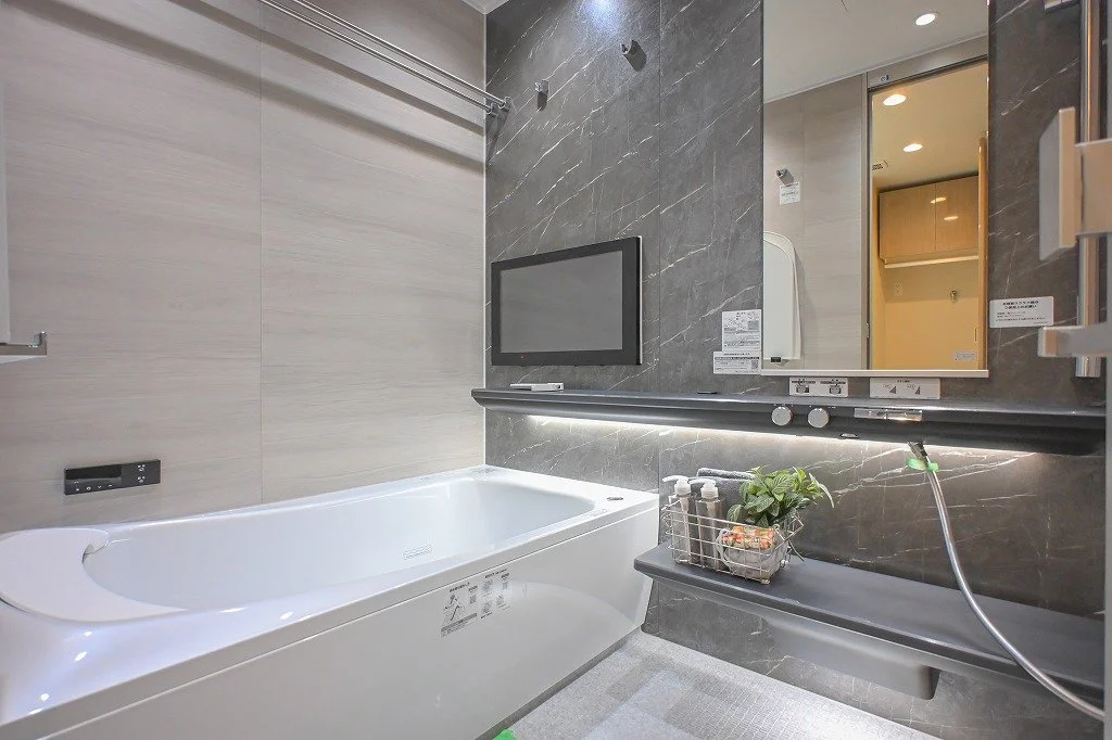 モダンなバスルームの浴槽とテレビ、鏡とシャンプーなどの小物が置かれている