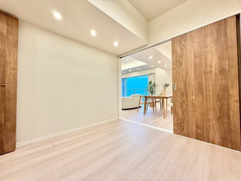 リビングルームの写真で、木製のスライドドアが開いており、向こう側に白いソファとテーブルが見える。大きな窓から自然光が入っている。