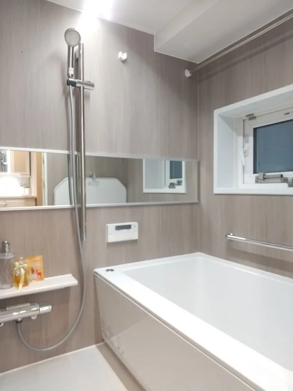 モダンな浴室。バスタブとシャワー、鏡と小さな窓がある。