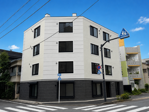 白い4階建ての建物と交差点の風景。
