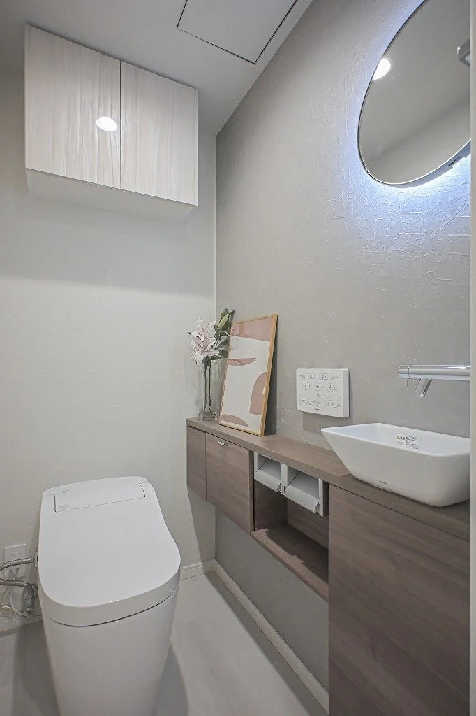 洗面所の室内で、トイレと洗面台があり、シンプルでモダンなデザインの空間。