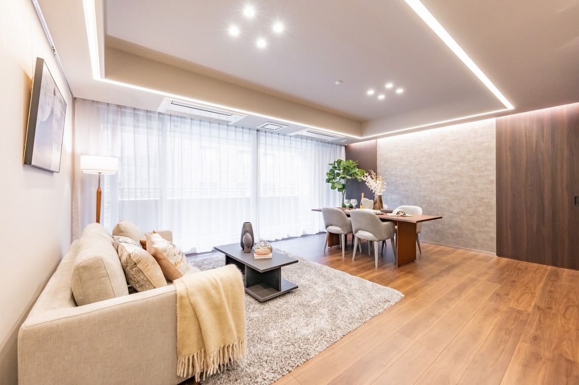 明るいリビングとダイニングルームの内装。ソファ、コーヒーテーブル、ダイニングテーブルと椅子、観葉植物、カーテンと照明が設置されている。