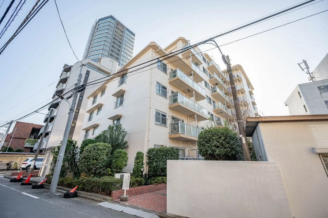 都市の住宅街にある白い中層マンションとその周辺の植栽