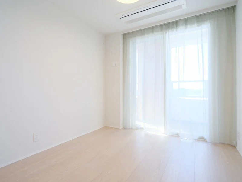 白い壁と薄い木の床、窓に白いカーテンがかかっている明るい部屋