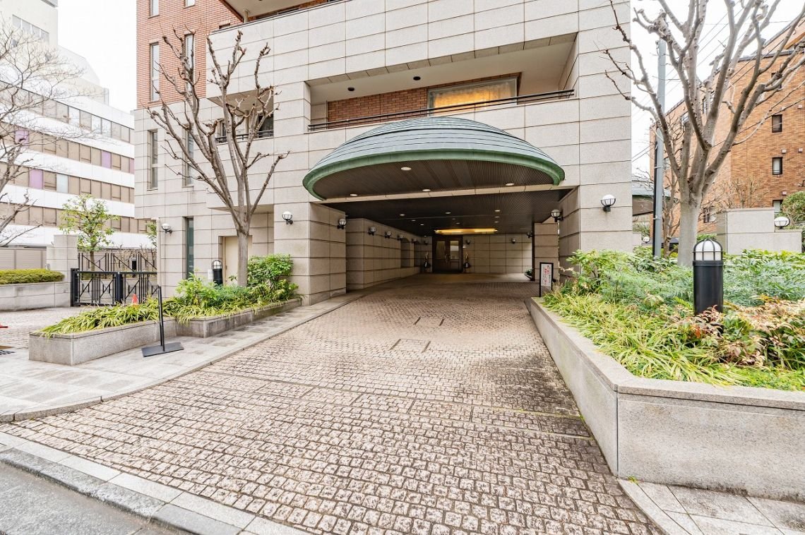 都市の建物の入り口付近と駐車場の入り口。周囲には幹のない木と植物が植えられている。