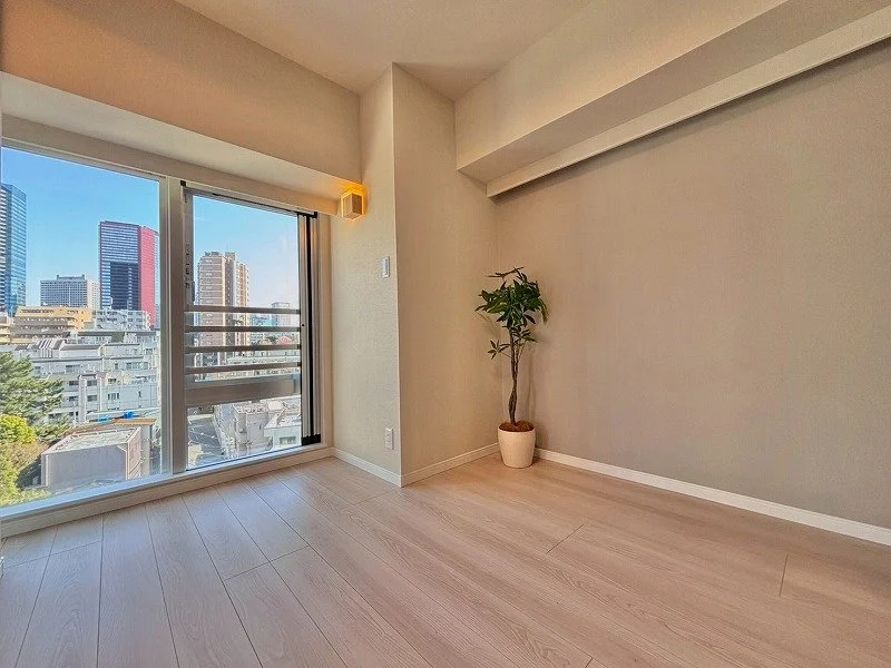 窓から都市のビル群が見える空いた部屋、壁に観葉植物。