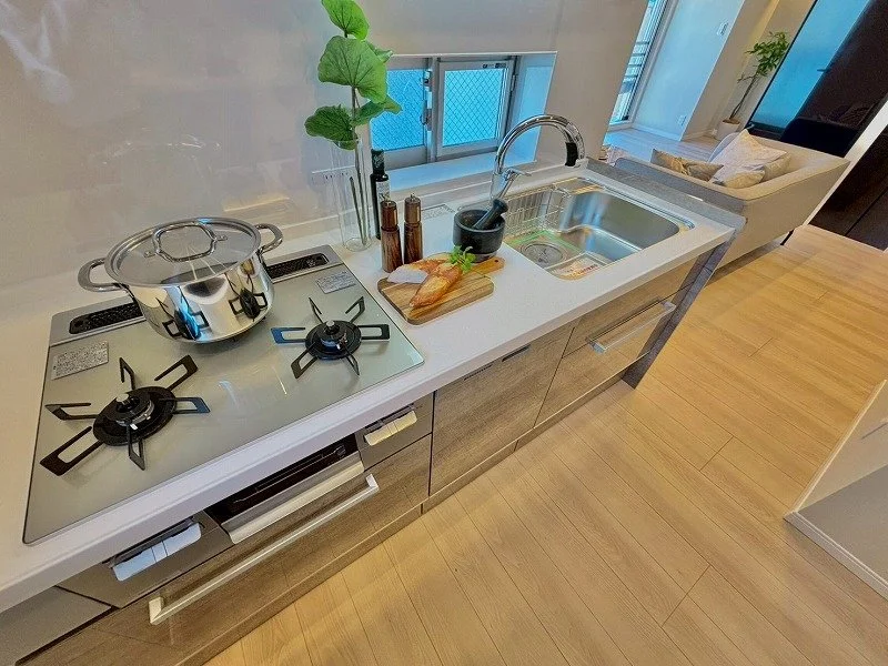 キッチンのカウンターにコンロとシンク、鍋と調味料、カッティングボードと包丁、飾りの植物があります。