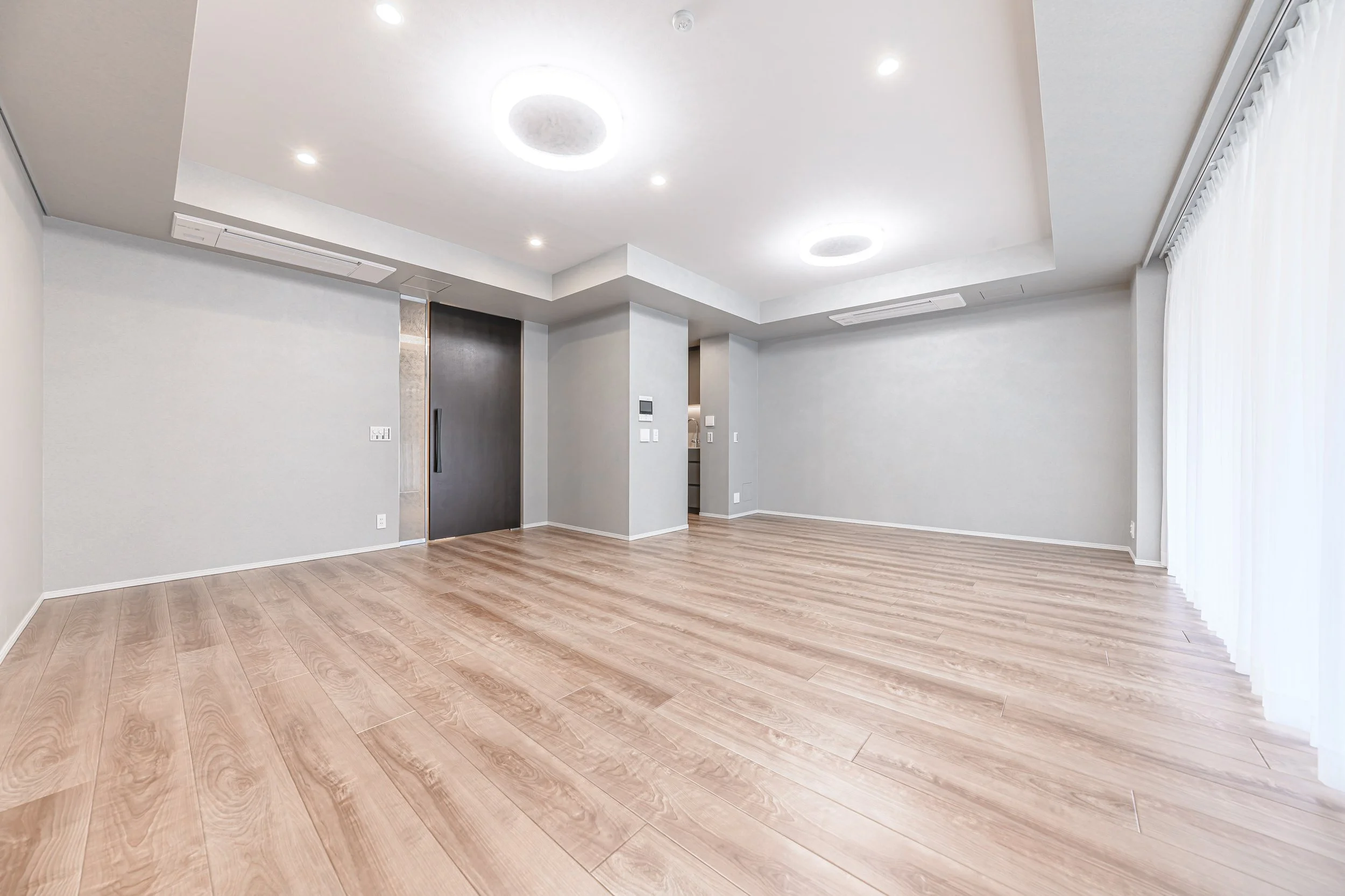 広々とした空間の無人のリビングルーム、白い壁と木製のフロア、天井に埋め込み照明と円形のライトが付いている