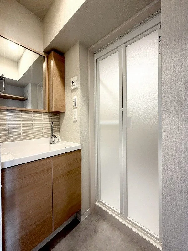 洗面台と鏡、ガラス扉の洗濯室の interior of a bathroom or washroom with a wooden cabinet and a mirror.