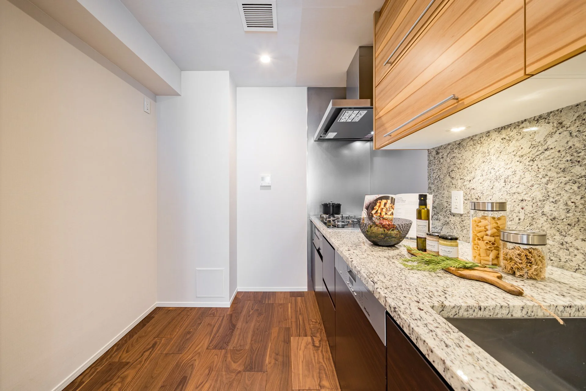 木目調の棚と大理石のカウンターが特徴的なキッチンの様子。キッチンには、調理用具や食材、調味料などが並んでいる。