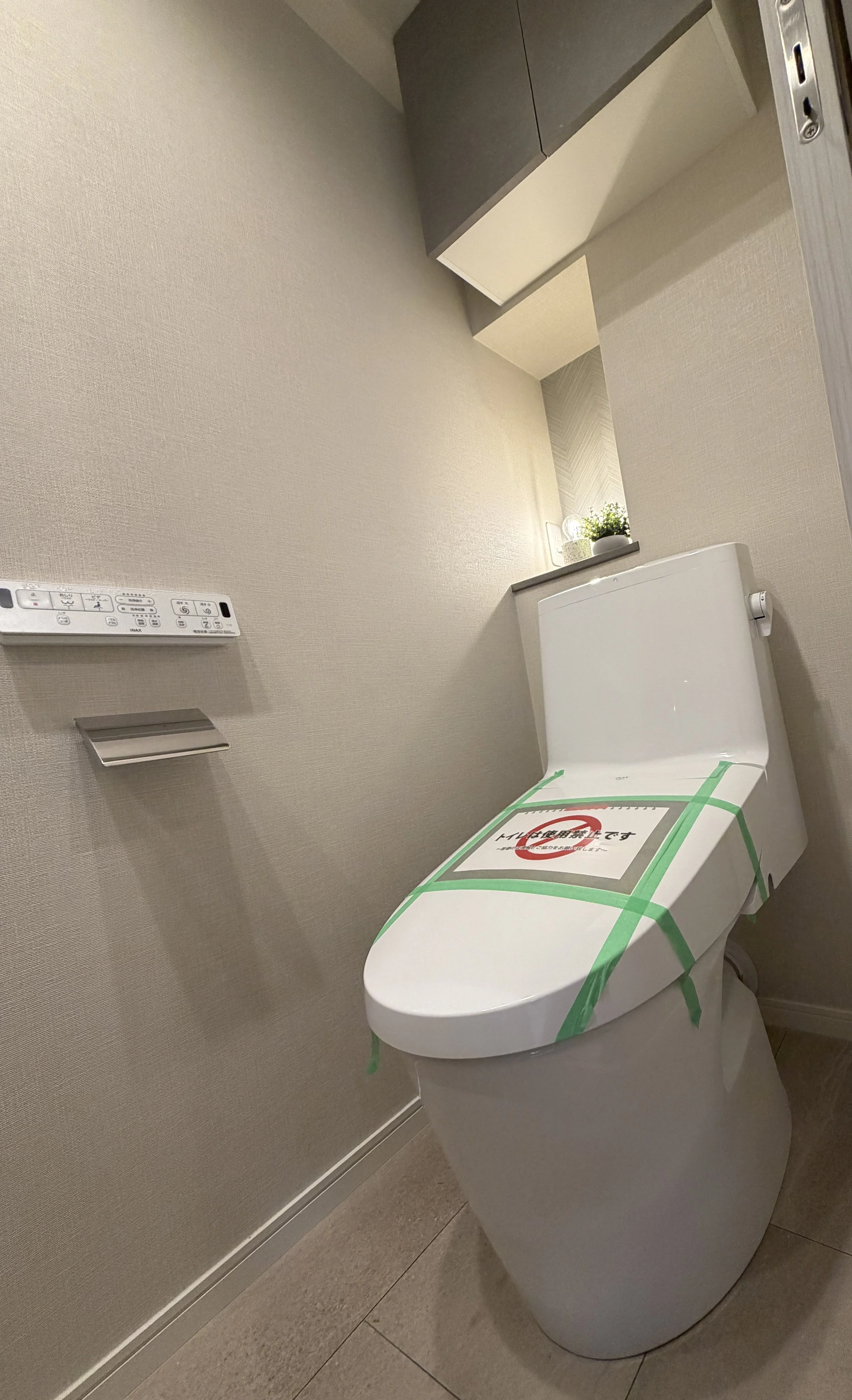 壁に取り付けられた清潔なトイレとトイレットペーパーホルダー、操作パネルと観葉植物の飾り。