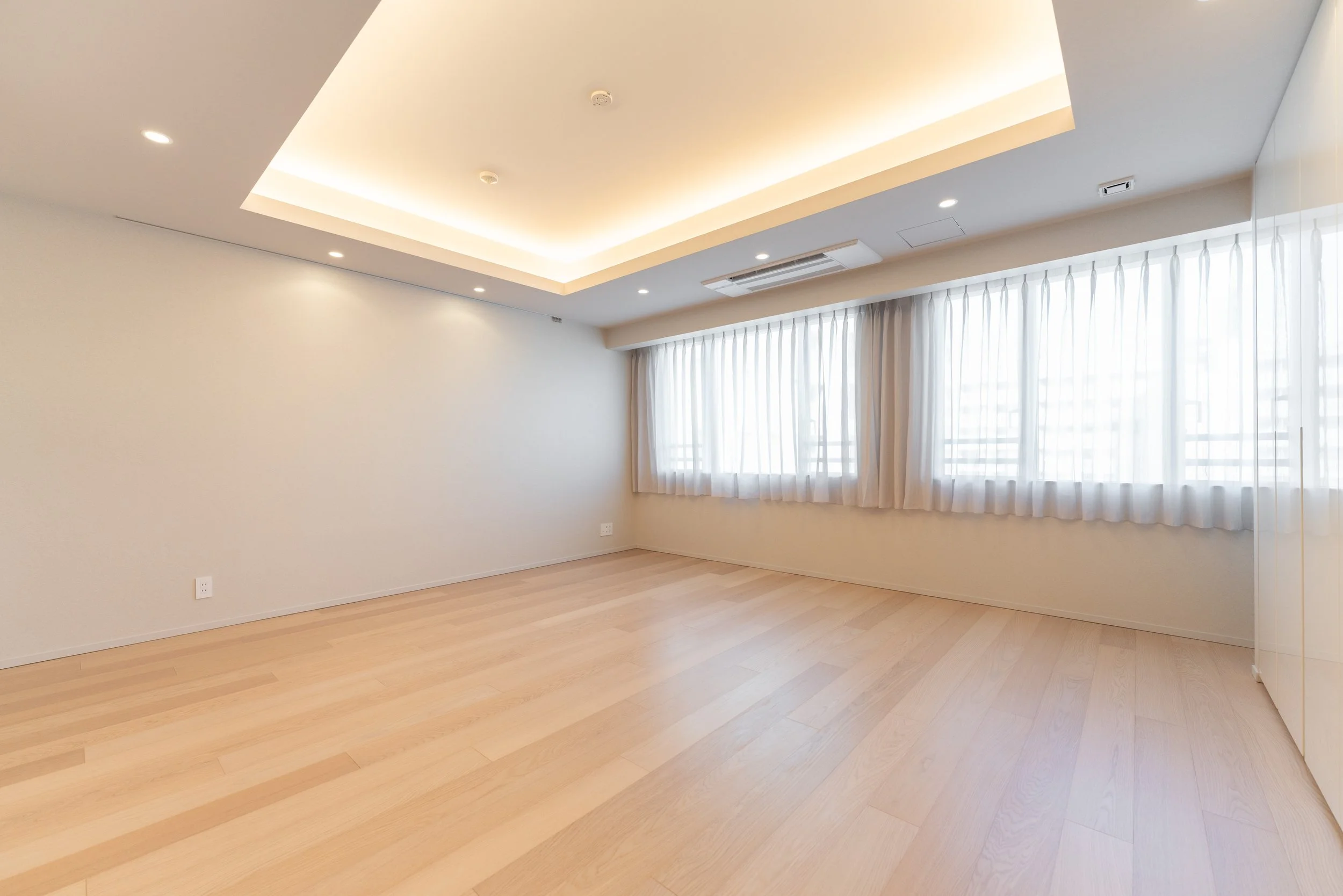 白い壁と大きな窓に白いカーテンを引いた空の部屋。天井に間接照明とエアコンが設置されている。木目調のフローリング。」}】}‹|endoftext| 
