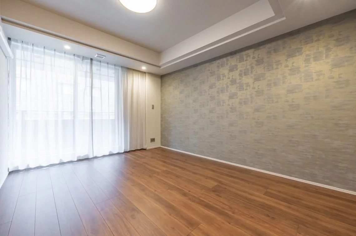 白いカーテン越しに自然光が差し込む空の部屋、木製の床と壁の一部が石のような模様のアクセントウォールになっている