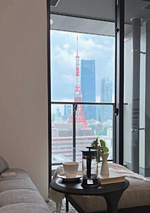 都心の高層ビルと東京タワーが見える窓際の室内風景、テーブルにコーヒーカップと植物。