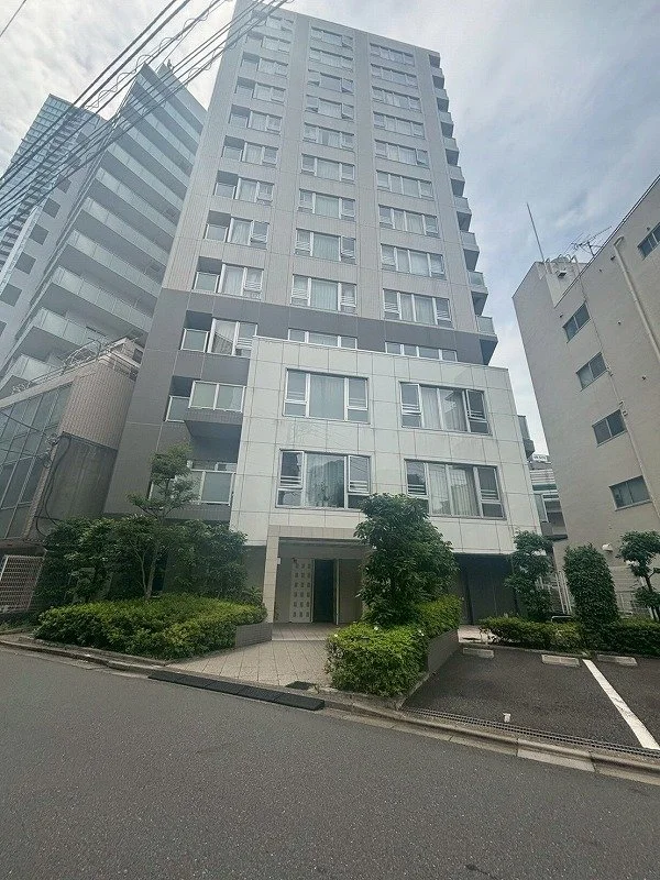 高層のマンションビルと、その前に植えられた樹木と低い生け垣。