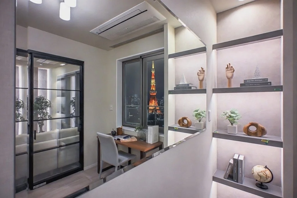 夜にライトアップされた東京タワーの景色が見える部屋の窓からの眺め。室内には本棚、植木、装飾品が飾られている。