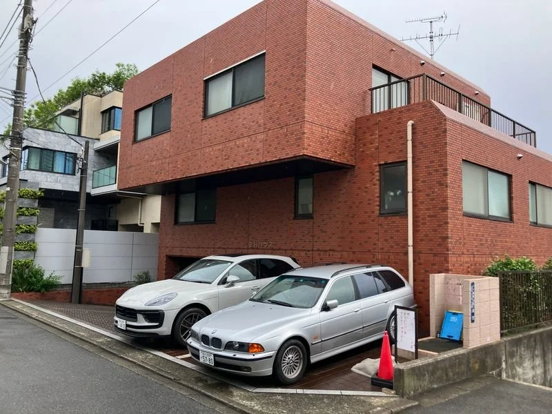 赤レンガ造りの三階建ての建物と駐車場に止められた白と銀色の車