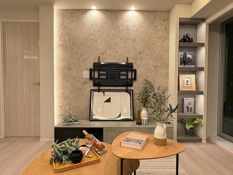 リビングルームの壁にテレビ台と飾り棚、テーブルの上に花と本、ワインとグラスが置かれている部屋の写真
