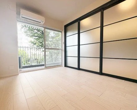 空の部屋で窓ガラスを通して木のある景色が見える。室内にはエアコンと仕切り戸がある。