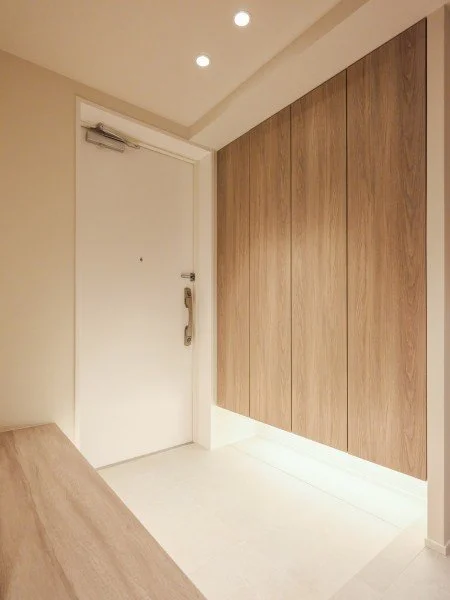 白いドアと木製の収納棚があるモダンな室内のエントランスホール