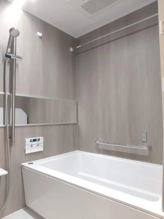 バスタブとシャワー設備のある浴室の内部。壁は木目調のパネル、鏡と手すりが設置されている。