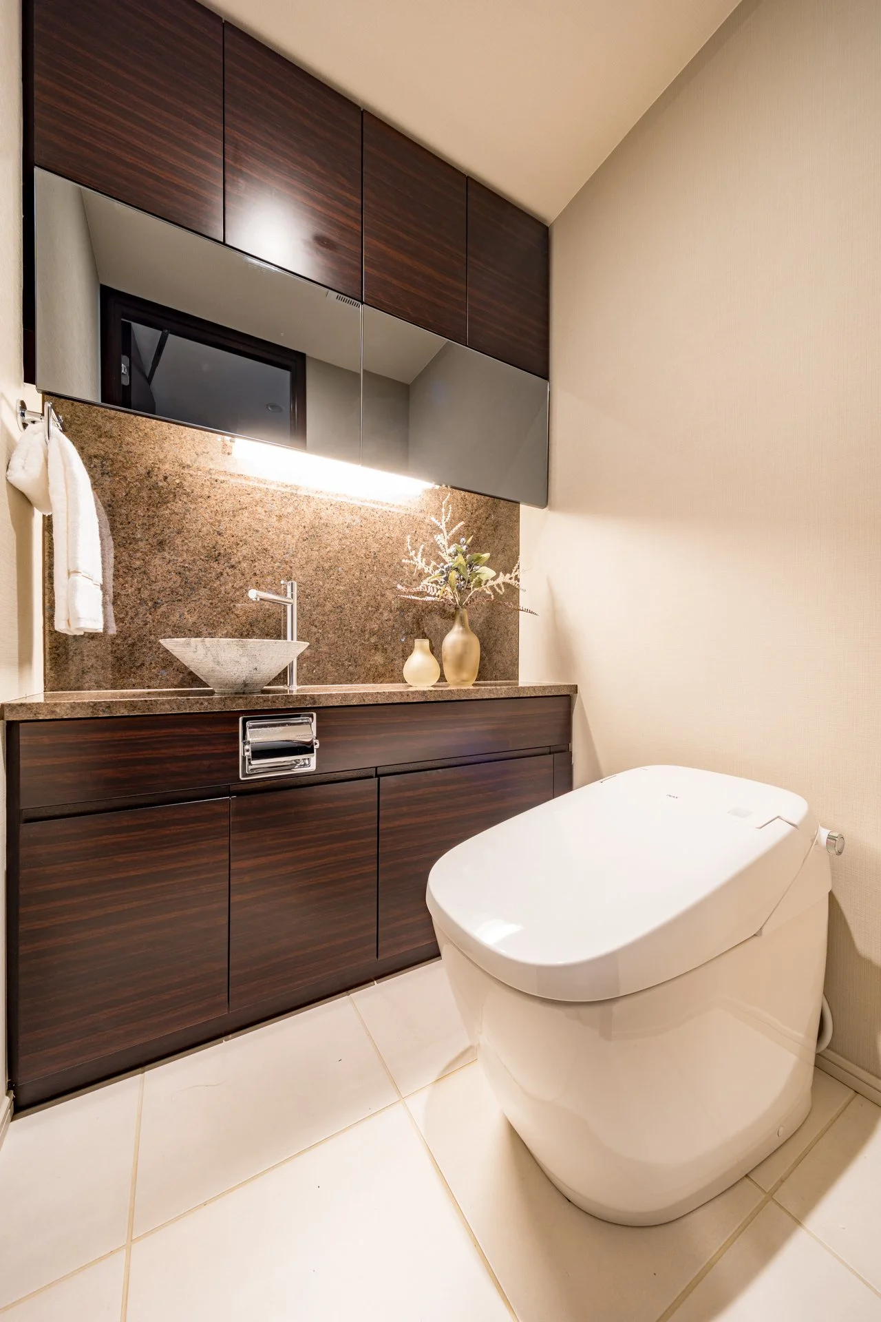 洗面台とトイレがあるモダンなバスルームのInterior写真。木製のキャビネットと鏡、花の飾りがある。