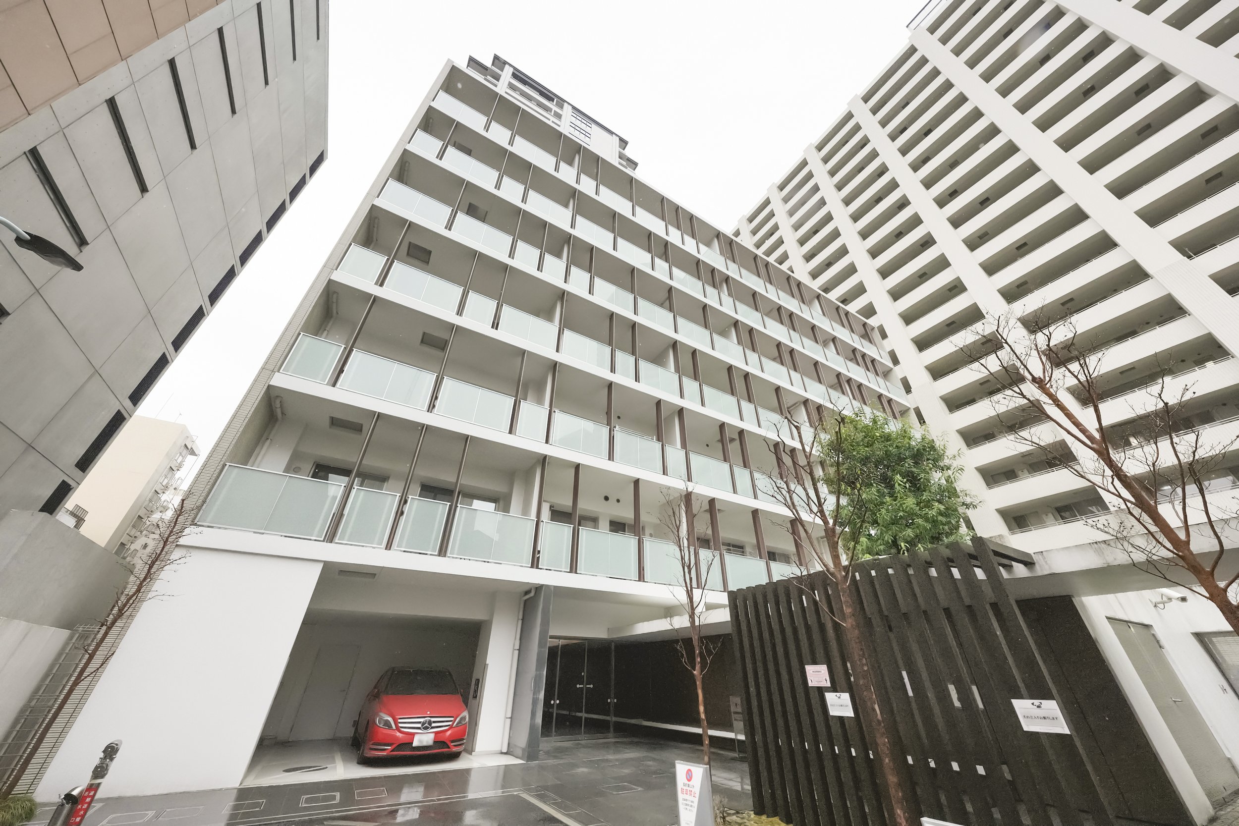 都市の高層アパートメントの建物と駐車場に赤い車が停まっている様子