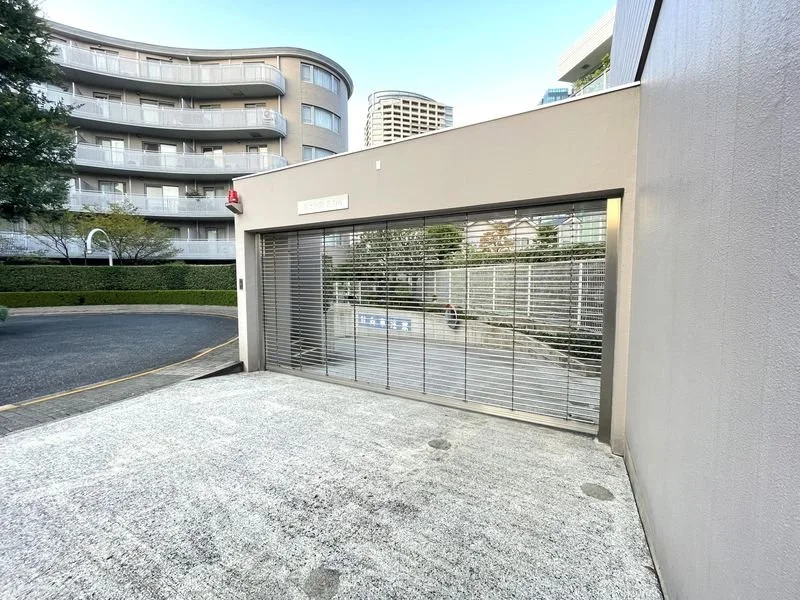 閉まった金属のゲートと高層マンションが写っている都市のエントランス（車止めと道路も見える）