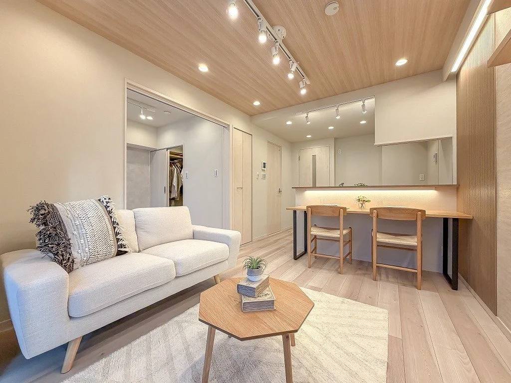 木目調の天井と床のリビングルームに白いソファと丸い木製のコーヒーテーブル、カウンター席の椅子が配置されている。シンプルで温かみのあるインテリアです。