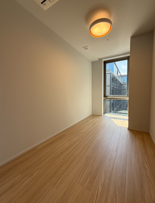 日光が入る空室の部屋、木製フローリング、天井の照明、バルコニーへの窓