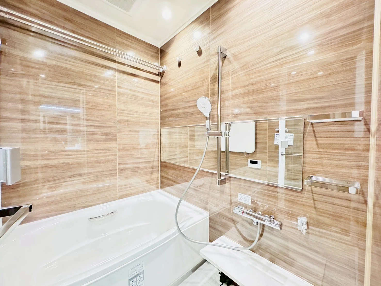 木目調の浴室、シャワーヘッドとバスタブ、鏡と棚が設置されている