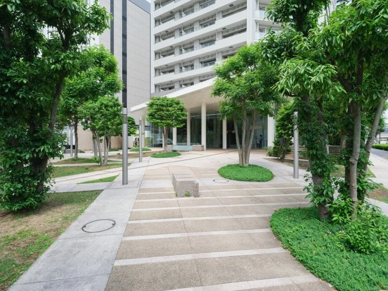 高層ビルの前に緑が多い散策路と植え込みがあるモダンな都市公園