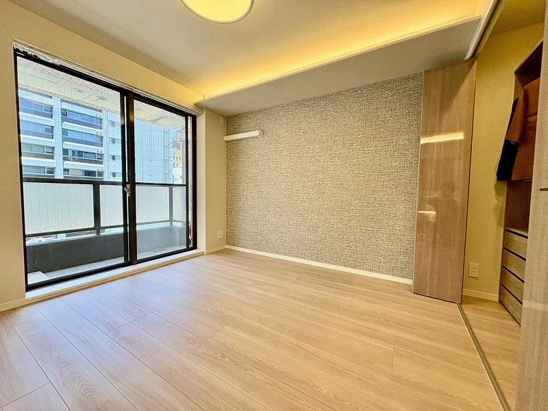 日当たりの良い空の広い空間で、木製の床と壁紙が特徴の部屋。大きな窓から都市の景色が見える。