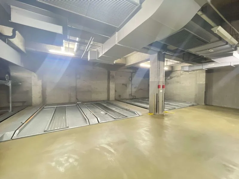 地下の駐車場の車両リフトと換気ダクト。コンクリートの壁と床、照明付き。