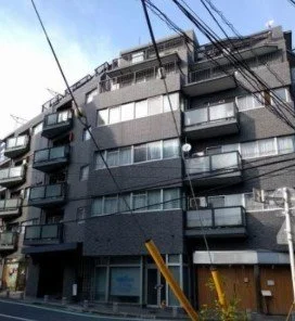黒い外観の中層コンクリートマンション。ベランダと窓があり、電線が前面を横切っている。