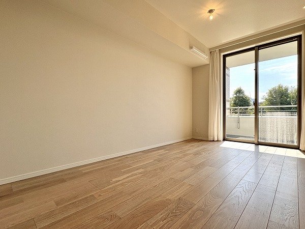 空の部屋の角からの写真で、木製の床と窓があり、外に木や空が見える