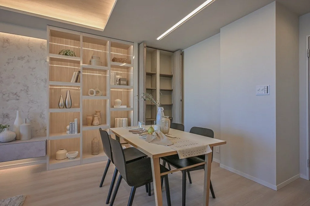 ダイニングルームの内部、木製のテーブルと黒い椅子、壁に白と木の棚と飾り皿や花瓶、照明とシンプルなインテリア