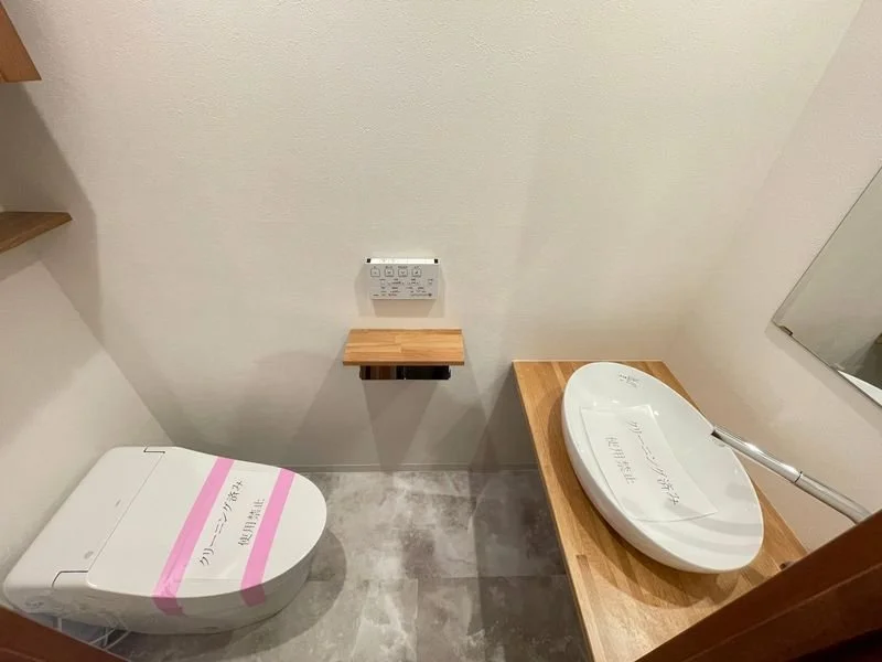 清潔で現代的なトイレルームの写真、木製のカウンターに設置された洗浄機付き便座、壁にリモコンと小さな棚がある