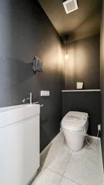 黒い壁のトイレルームに便座と洗面台がある
