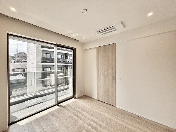 空の部屋で、壁は白色、木製のスライドドアと大きなガラス窓がある。