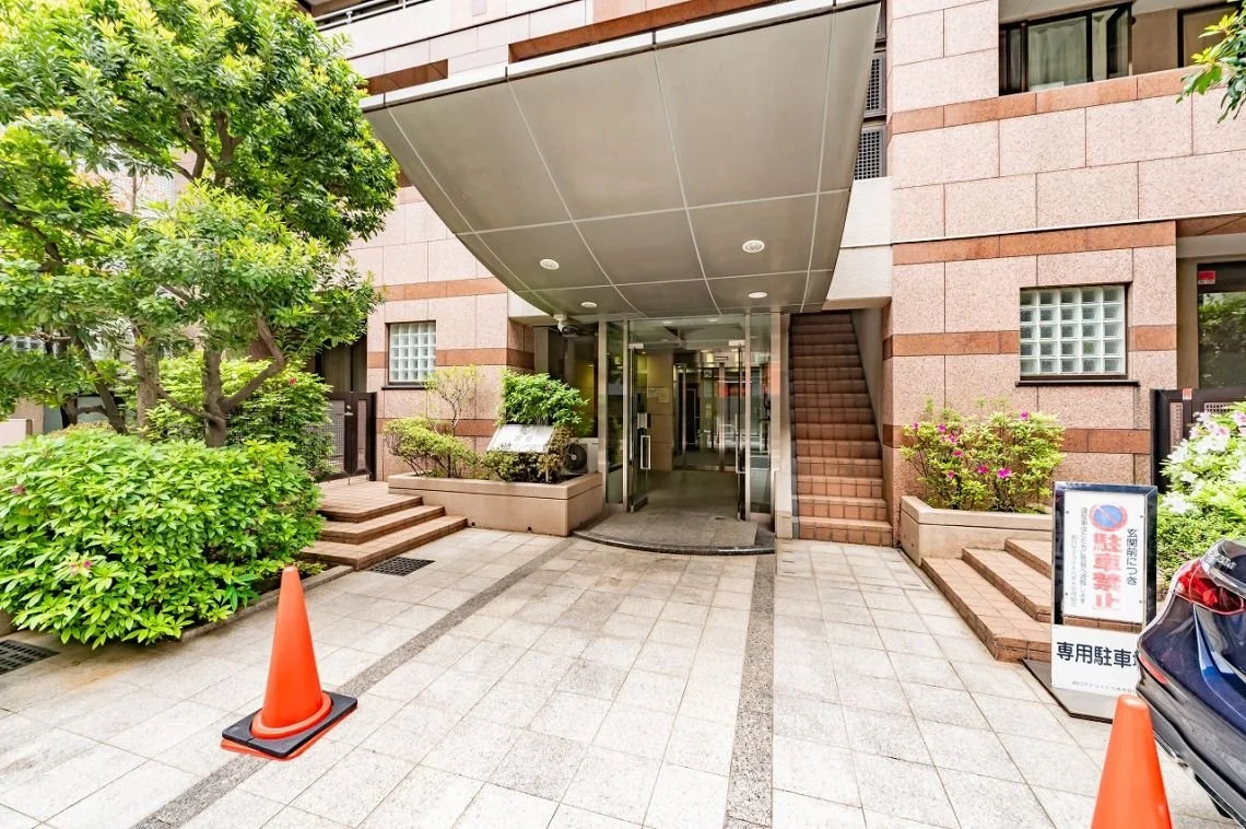 建物のエントランス入口と周囲の植栽、案内板と駐車禁止の看板がある駐車スペース