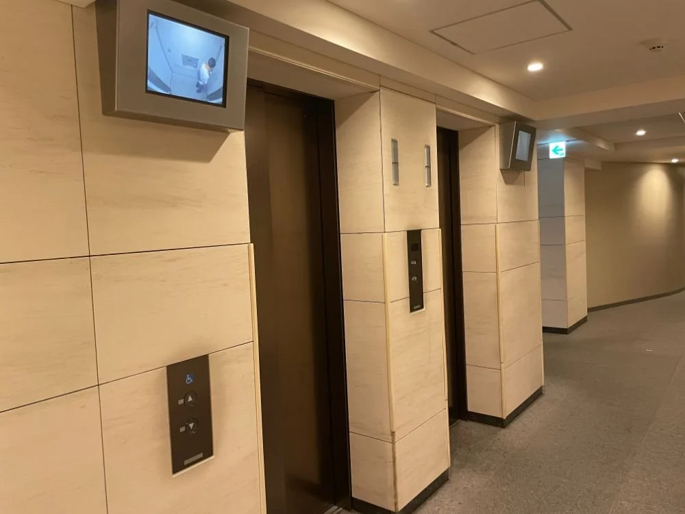 ホテルのエレベーターが並んでいるロビーの壁に設置されたモニターとエレベーターボタン。