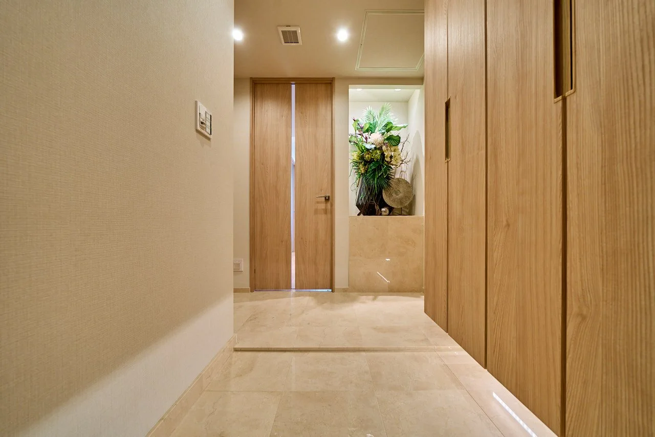 木製の扉と壁に囲まれた、明るく整頓された玄関ホールに花の飾りが置かれた空間